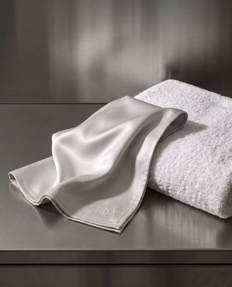 A smooth SEDA silk face cloth beside a folded cotton terry towel, showing the difference between a flat charmeuse weave and a raised looped pile